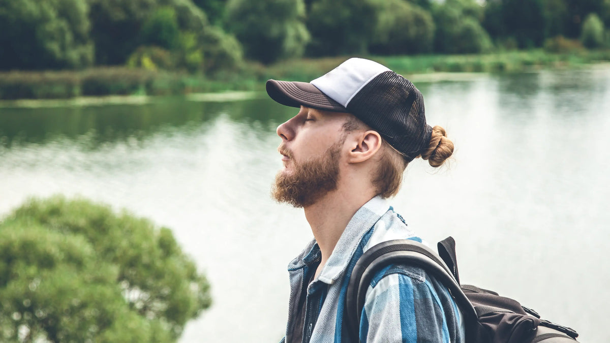 Man wearing a funny fishing trucker hat outdoors near the water